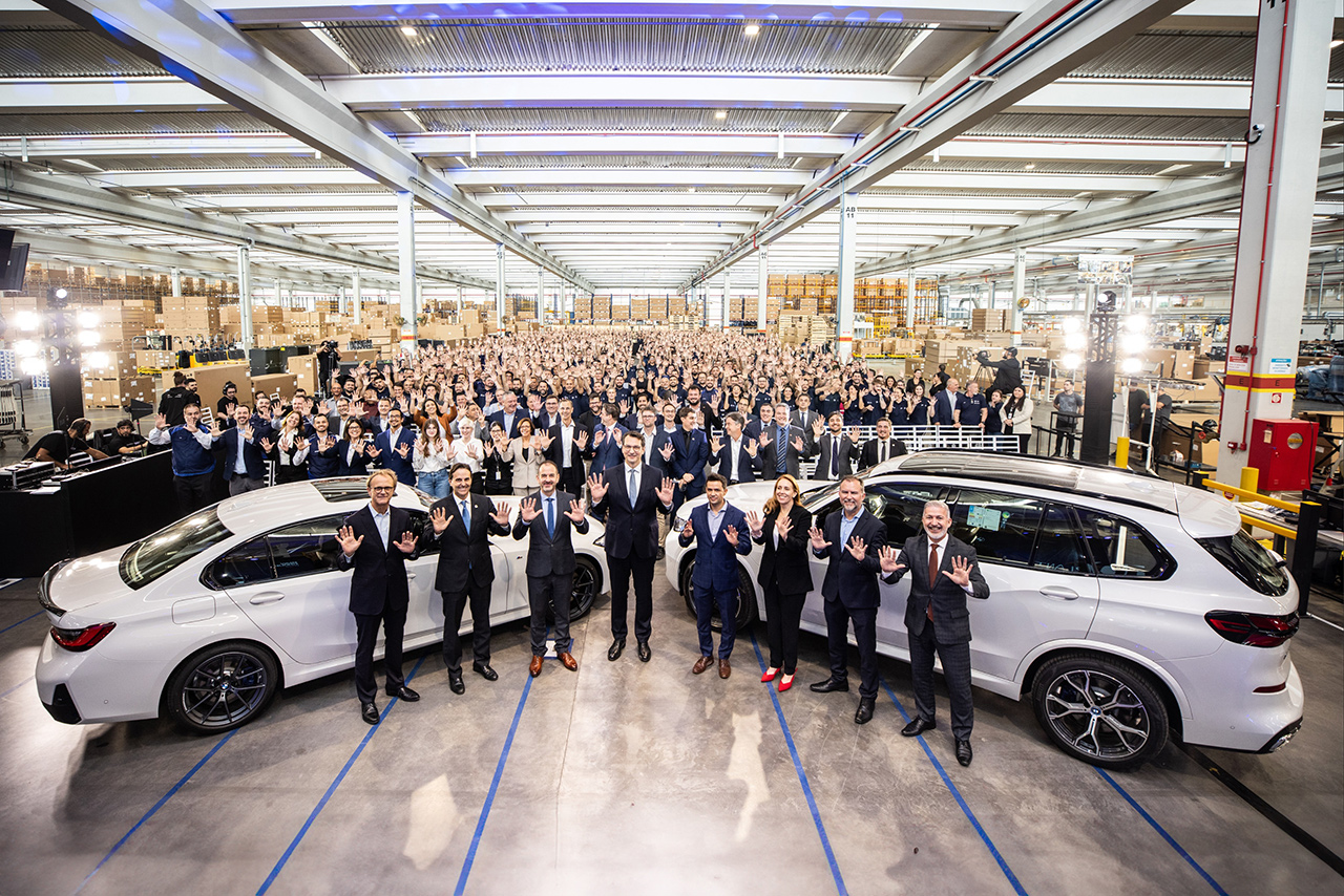 A Group of the Leadership team positing together with two white BMW cars and the whole team in the BMW Plant.