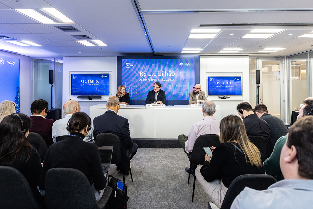 Three board members hold a press talk infront of a smaller group of people.