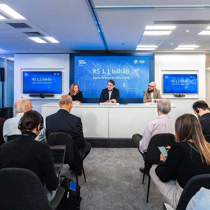 Three board members hold a press talk infront of a smaller group of people.
