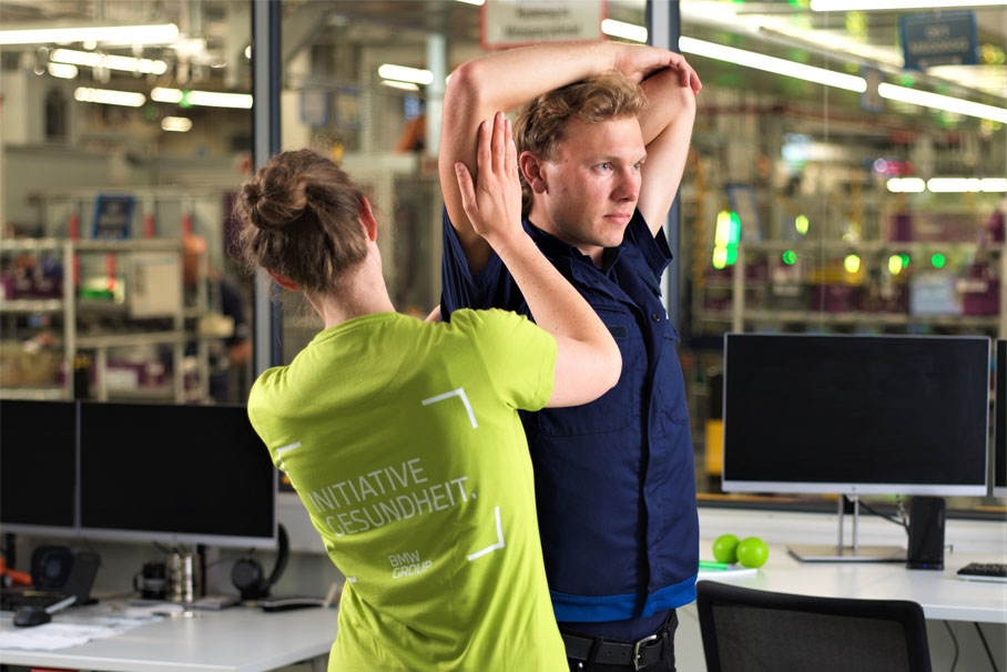 Eine junge Dame macht Dehnungsübungen mit einem Mitarbeiter in der Produktion.