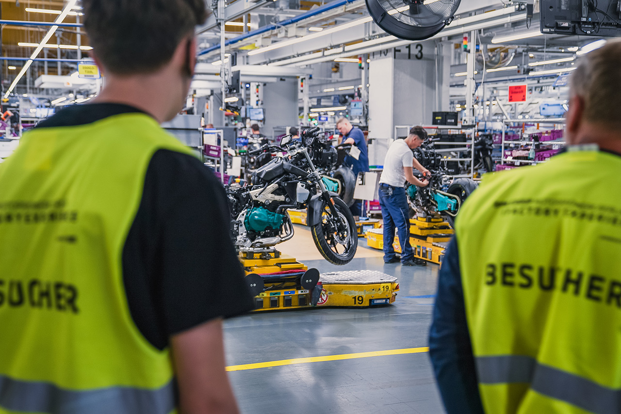 Besucher des BMW Group Werks Berlin schauen bei der Montage von BMW Motorrädern zu.