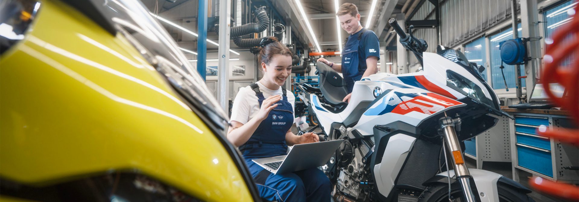 In einer Garage sind ein Mann und eine Frau mit der Arbeit an einem Motorrad beschäftigt.