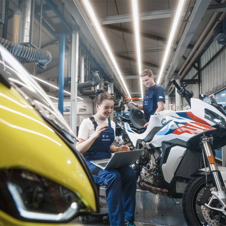 In einer Garage sind ein Mann und eine Frau mit der Arbeit an einem Motorrad beschäftigt.
