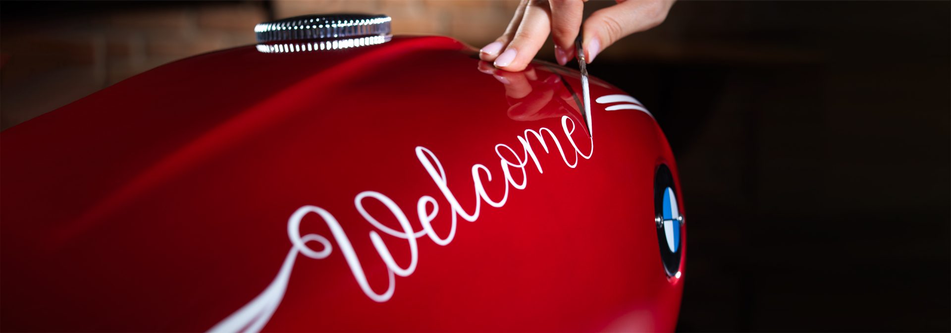 Roter BMW Motorrad Tank wird mit der weißen Aufschrift Welcome handbemalt.
