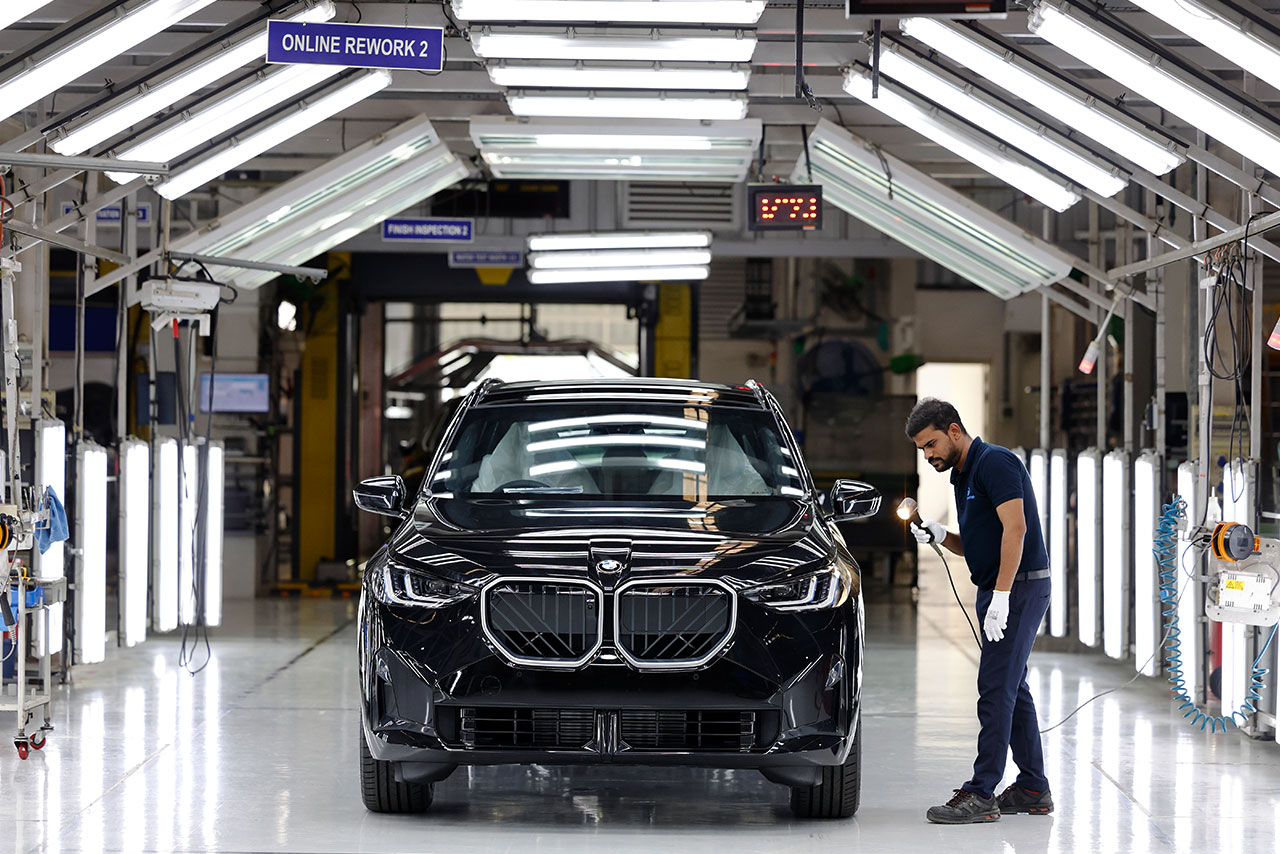 A worker inspecting a black BMW X3 in the modern BMW automotive manufacturing facility. 