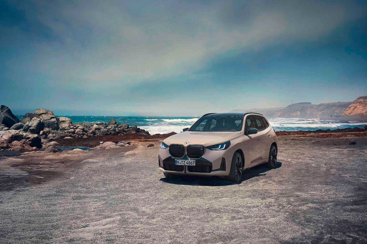  Tan colored BMW X3 standing on a gravel lot, with the sea in the background