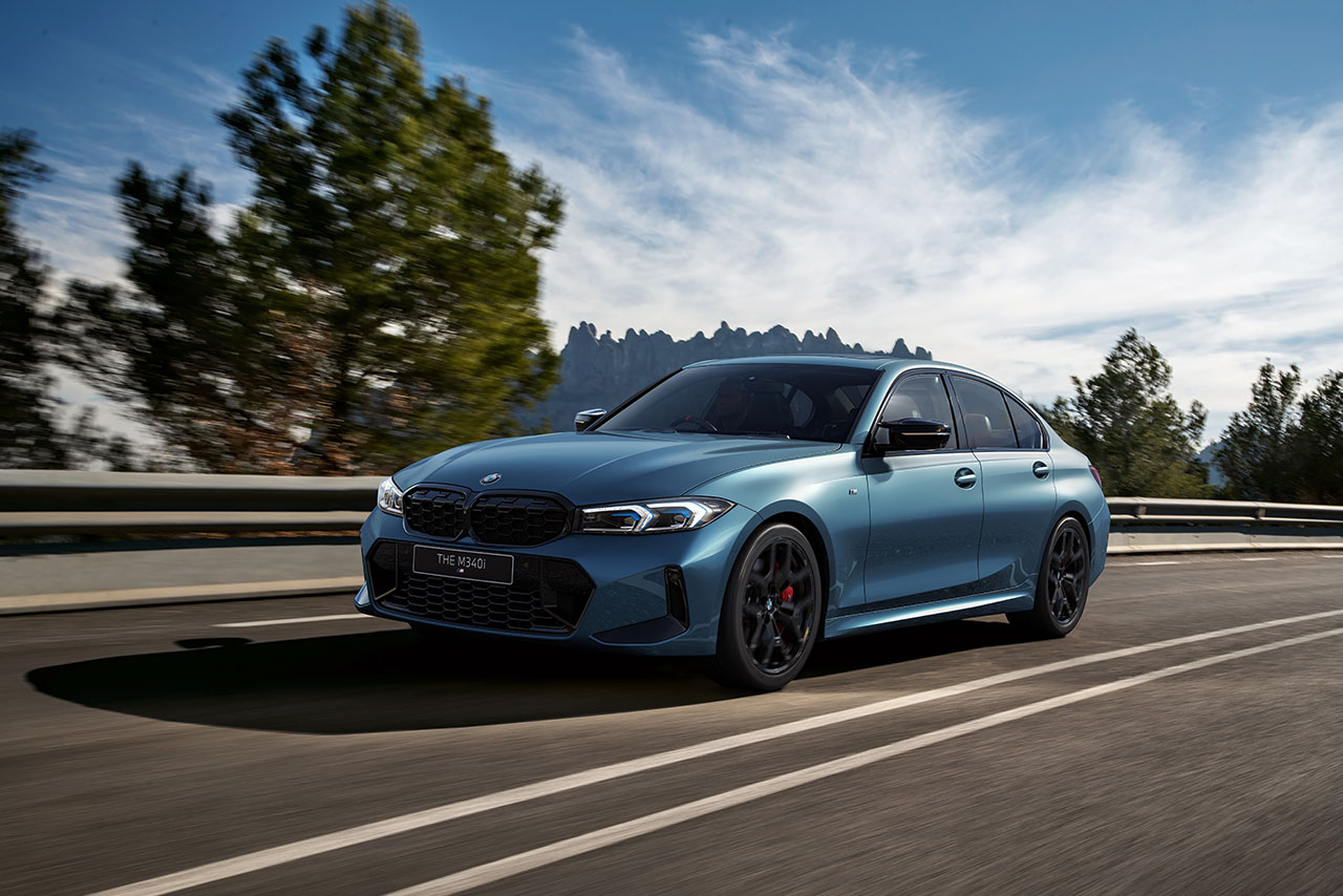  Light blue BMW M340i driving on a scenic road.