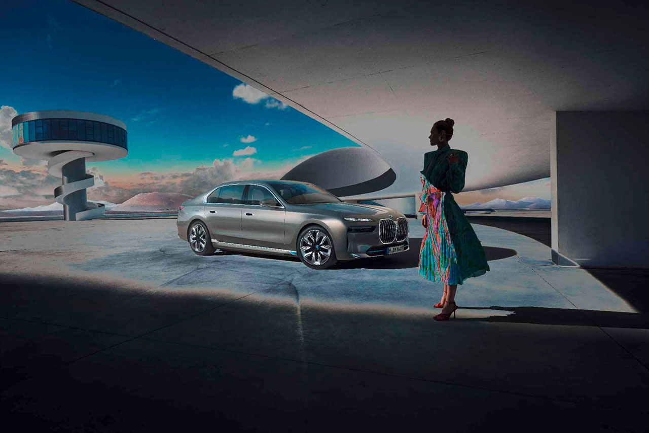 A woman in a stylish dress stands next to a grey BMW 7 series in a futuristic architectural setting.