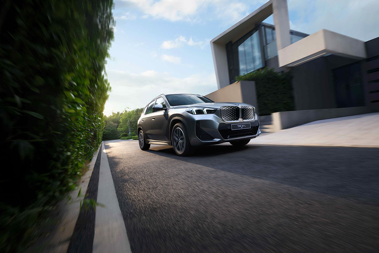 Grey BMW iX1 driving past a modern house. 