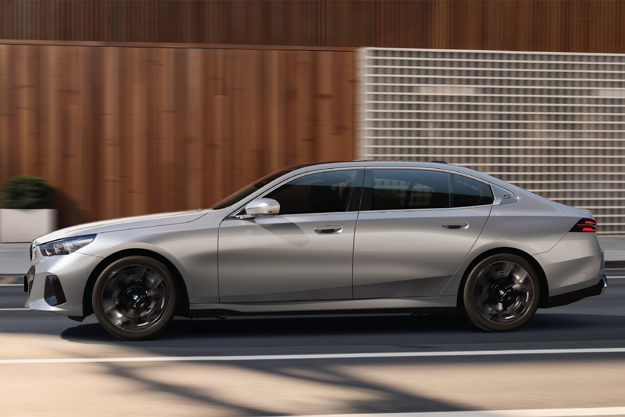 Side view of a silver sedan with black wheels in front of a wood and glass facade.