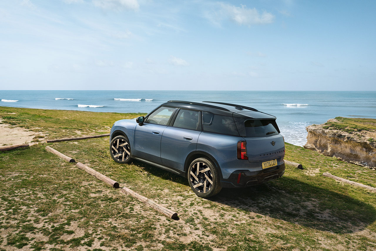 Two-tone MINI with large wheels parked on grassy area near the sea.