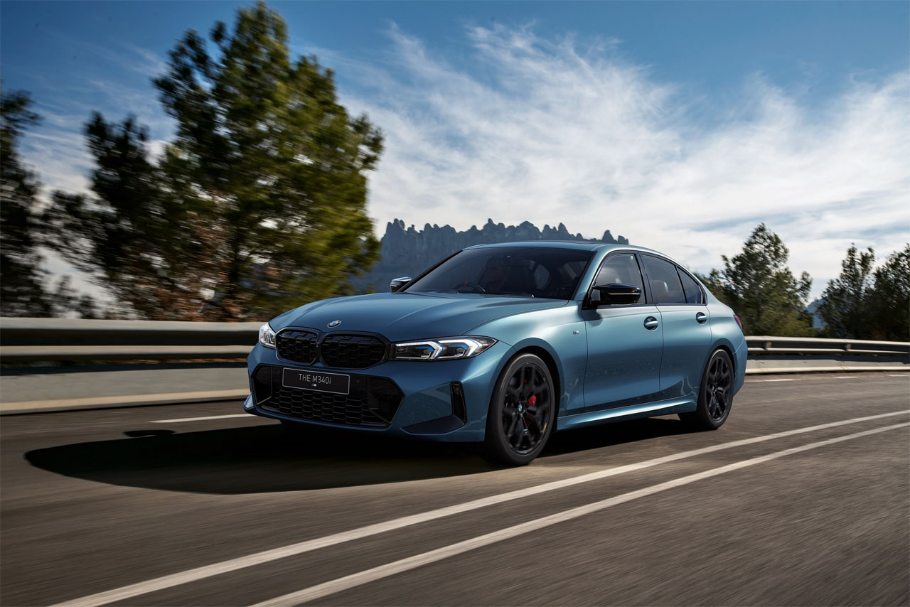 Blue BMW M340i driving on a winding road with trees in the background.