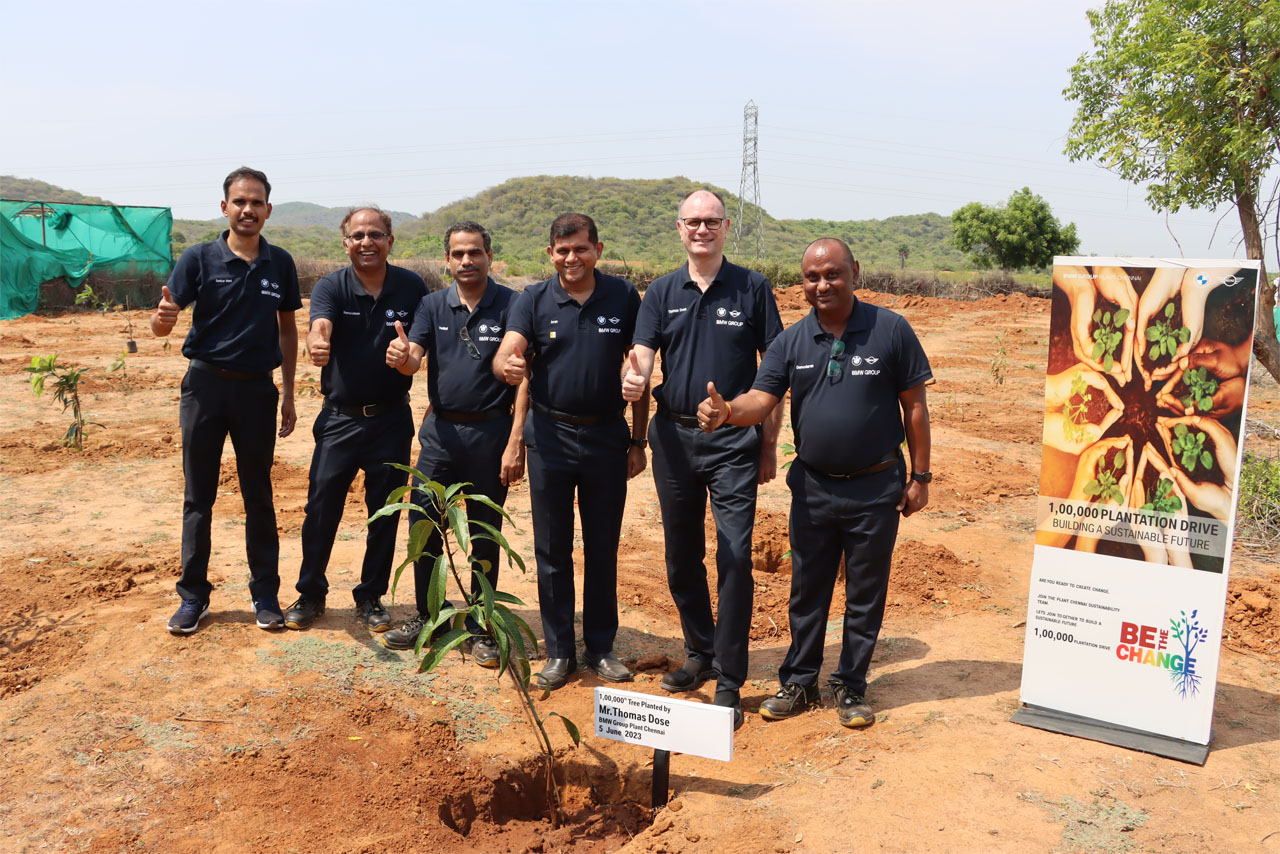 A cluster of men dressed in blue shirts stands near a tree, highlighting their unity in an outdoor environment.