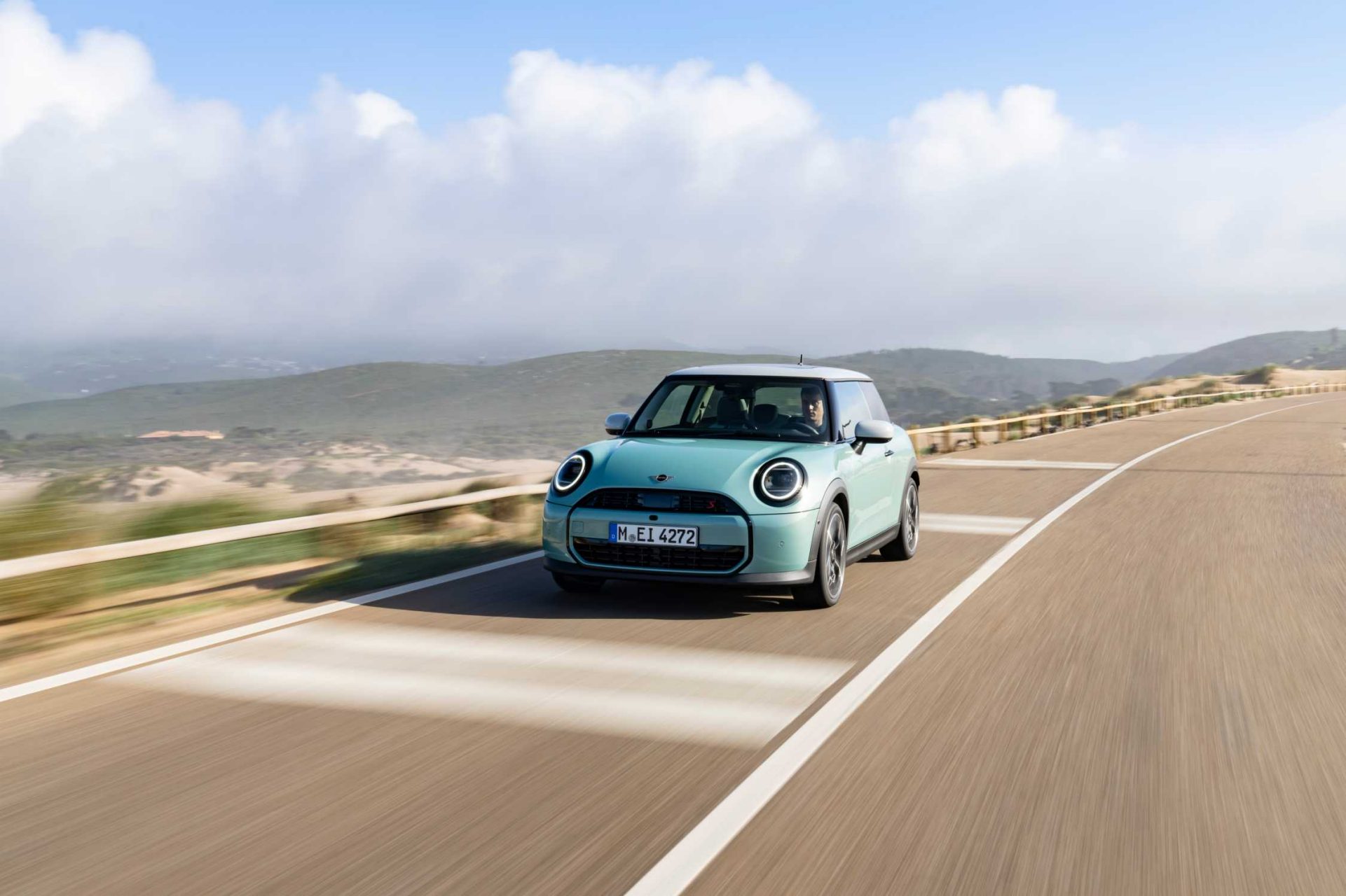  Mint colored Mini Cooper S driving on a scenic road.