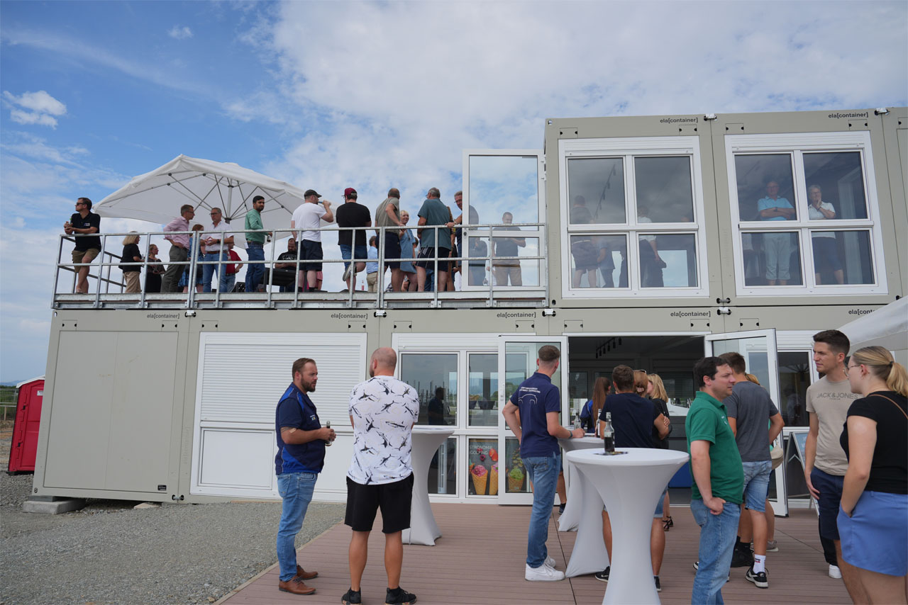  Menschen stehen auf dem Deck eines Containergebäudes und betrachten die Umgebung.