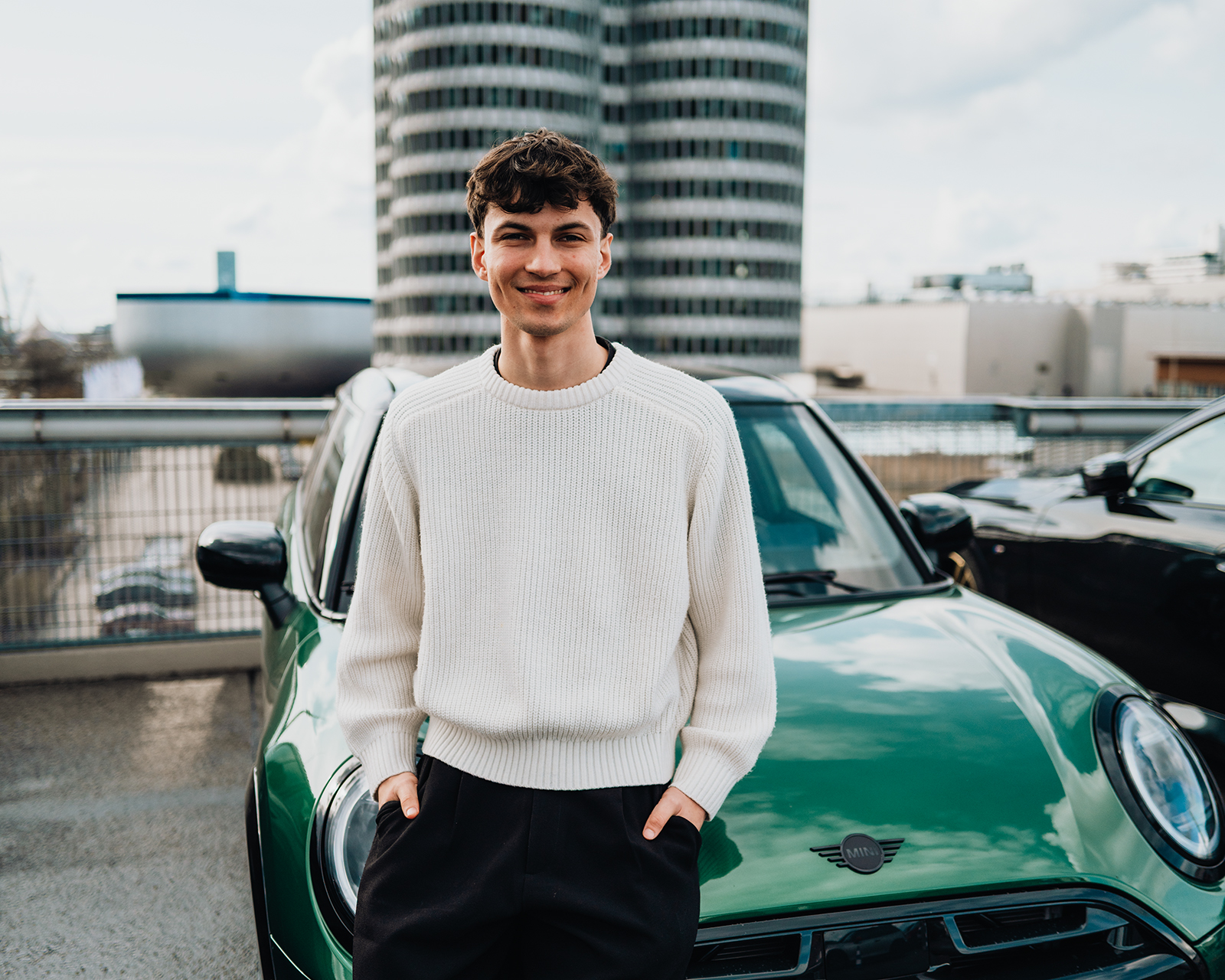Dualer Student Anton lehnt an einem grünen MINI vor dem BMW Vierzylinder