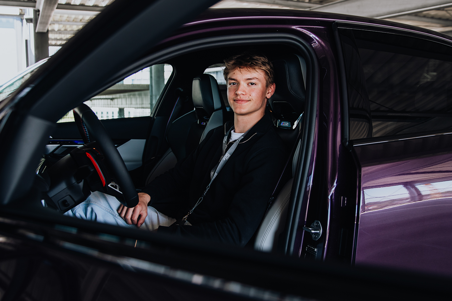 Azubi Tobias auf dem Fahrersitz eines BMW M5 in Lila