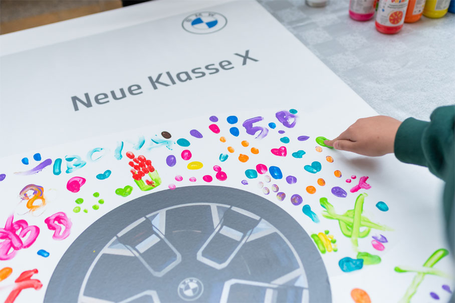 A child paints a wheel featuring the BMW logo, showcasing creativity and automotive enthusiasm.