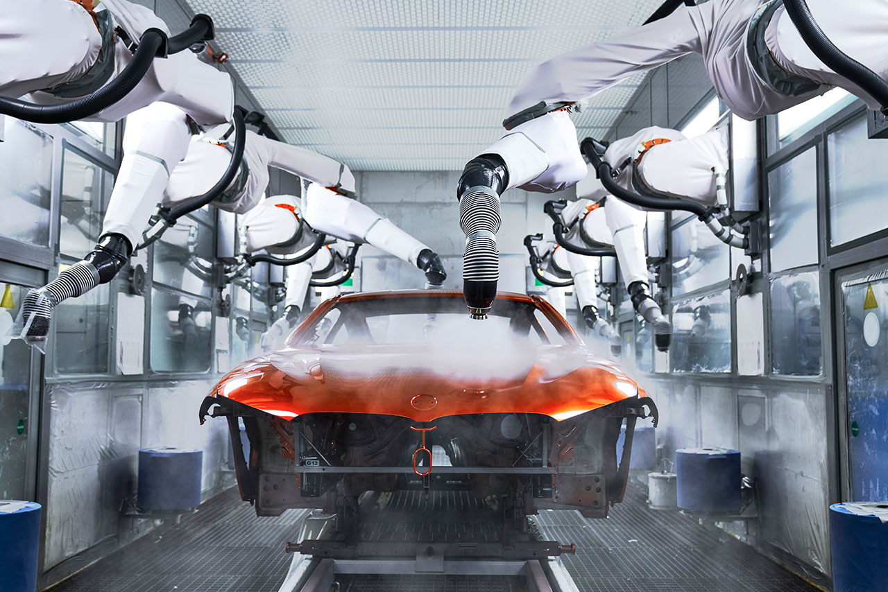 Multiple robot arms painting a car body orange.