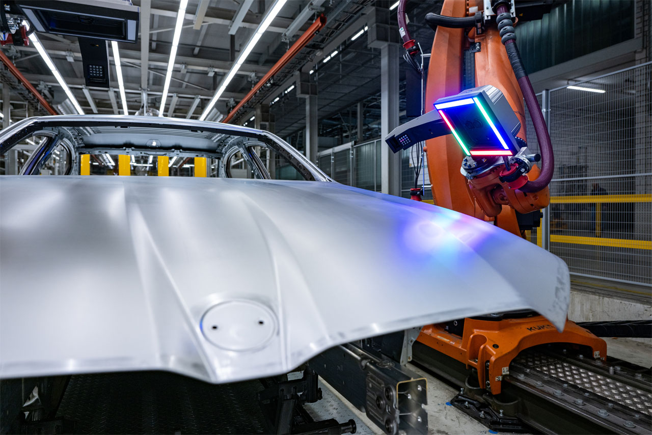 Industrieroboter mit leuchtendem Sensor scannt Motorhaube eines Autos in Fertigungshalle