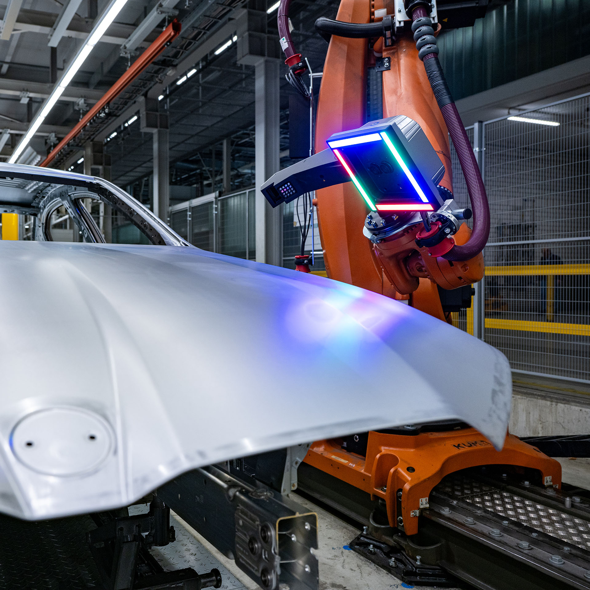Industrieroboter mit leuchtendem Sensor scannt Motorhaube eines Autos in Fertigungshalle