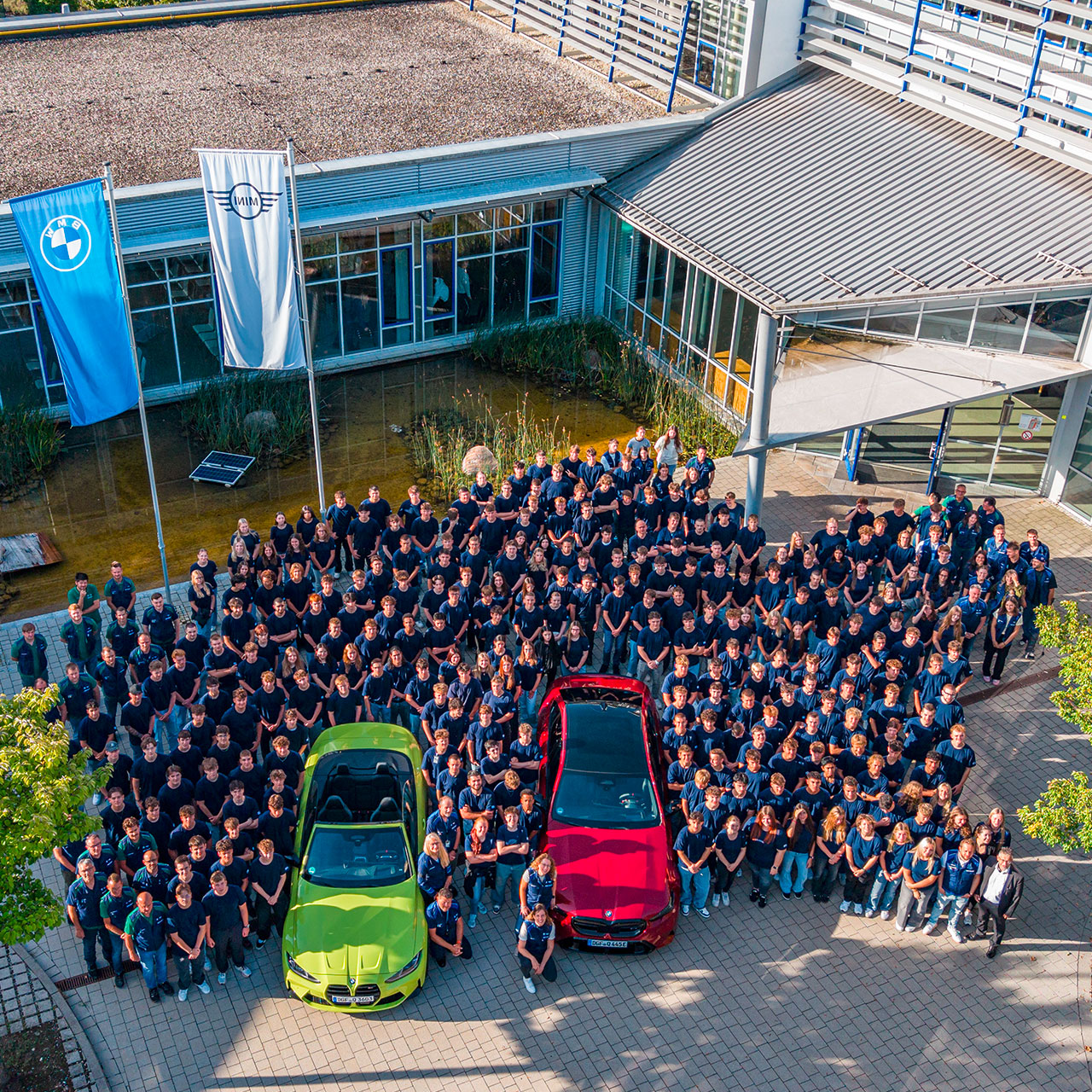 Gruppenfoto der neuen Azubis vor dem BMW Group Werk Steyr mit einem grünen und einem roten BMW Fahrzeug