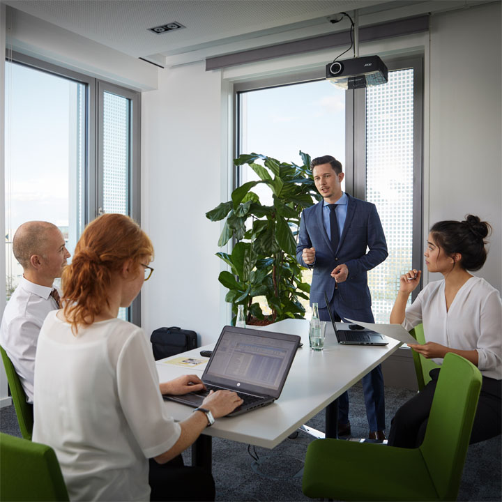 A man gives a lecture to three employees in a conference room.