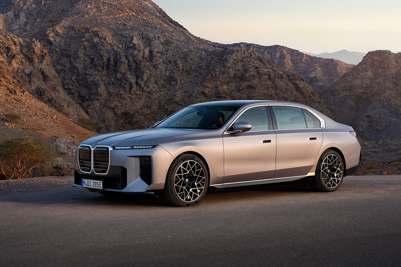 Silver BMW 7 with distinctive grille and intricate wheels in front of rocky mountains.