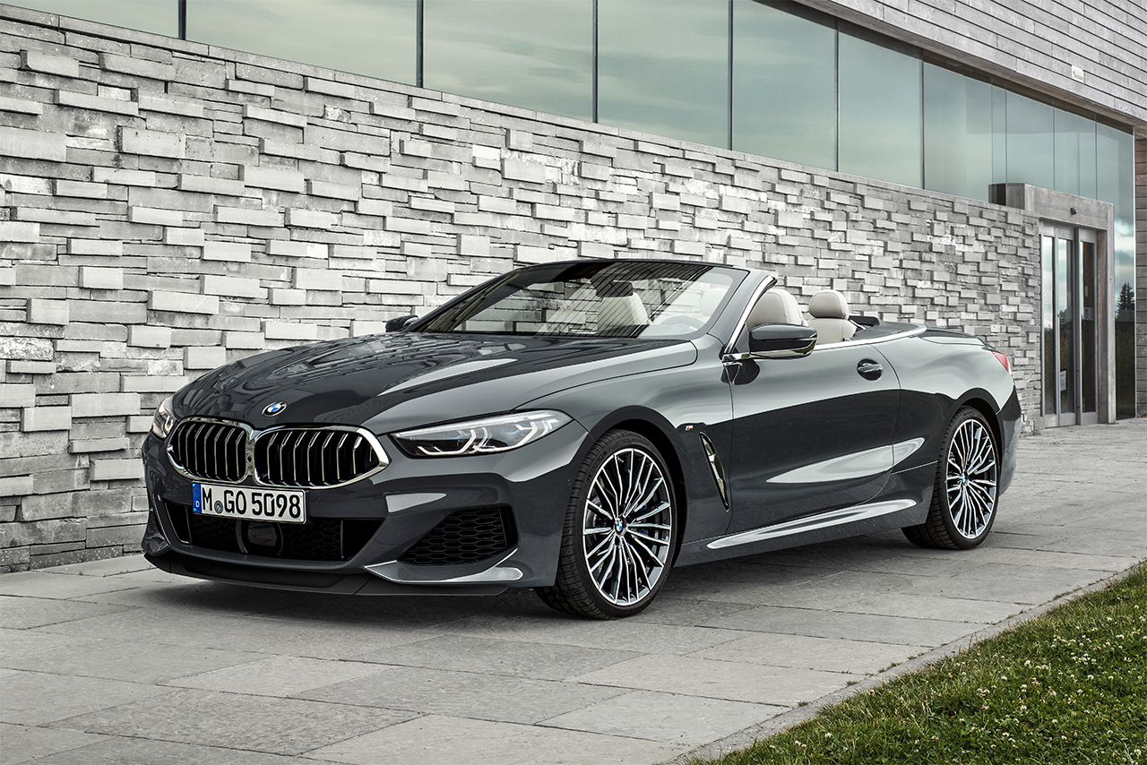 Greuer BMW 8 Series Convertible stands in front of a modern building with a stone facade.