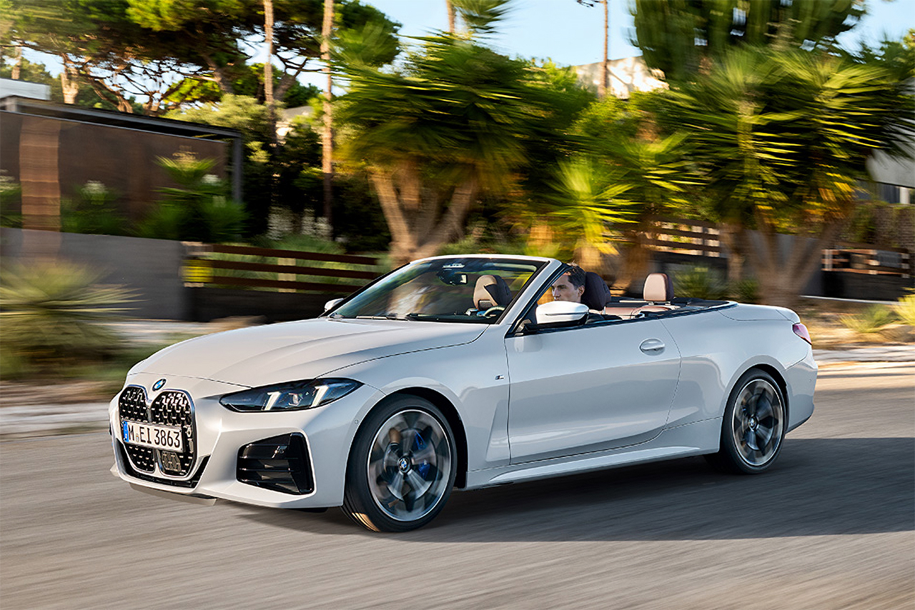 White BMW 4 Series convertible drives past palm trees on a road.