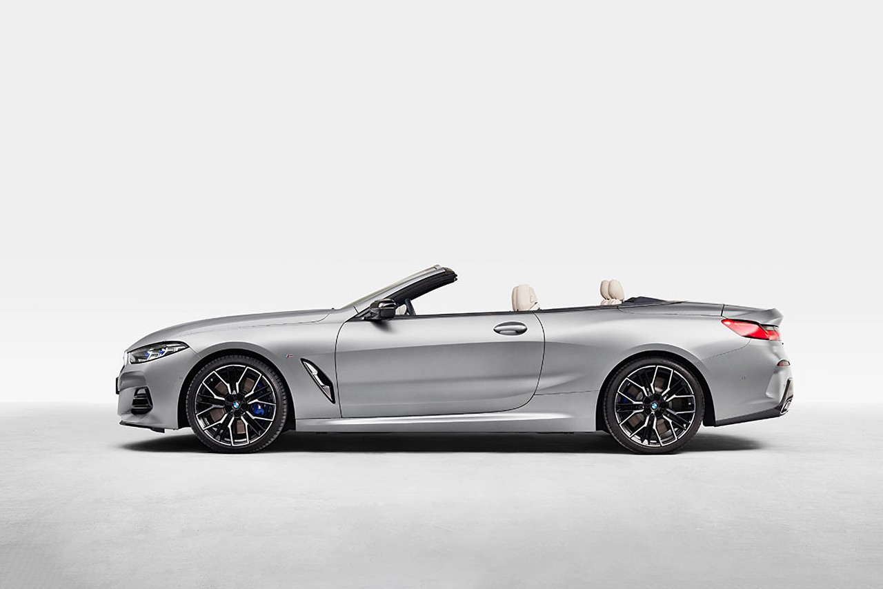 Silver BMW M8 convertible with open roof in a white room.
