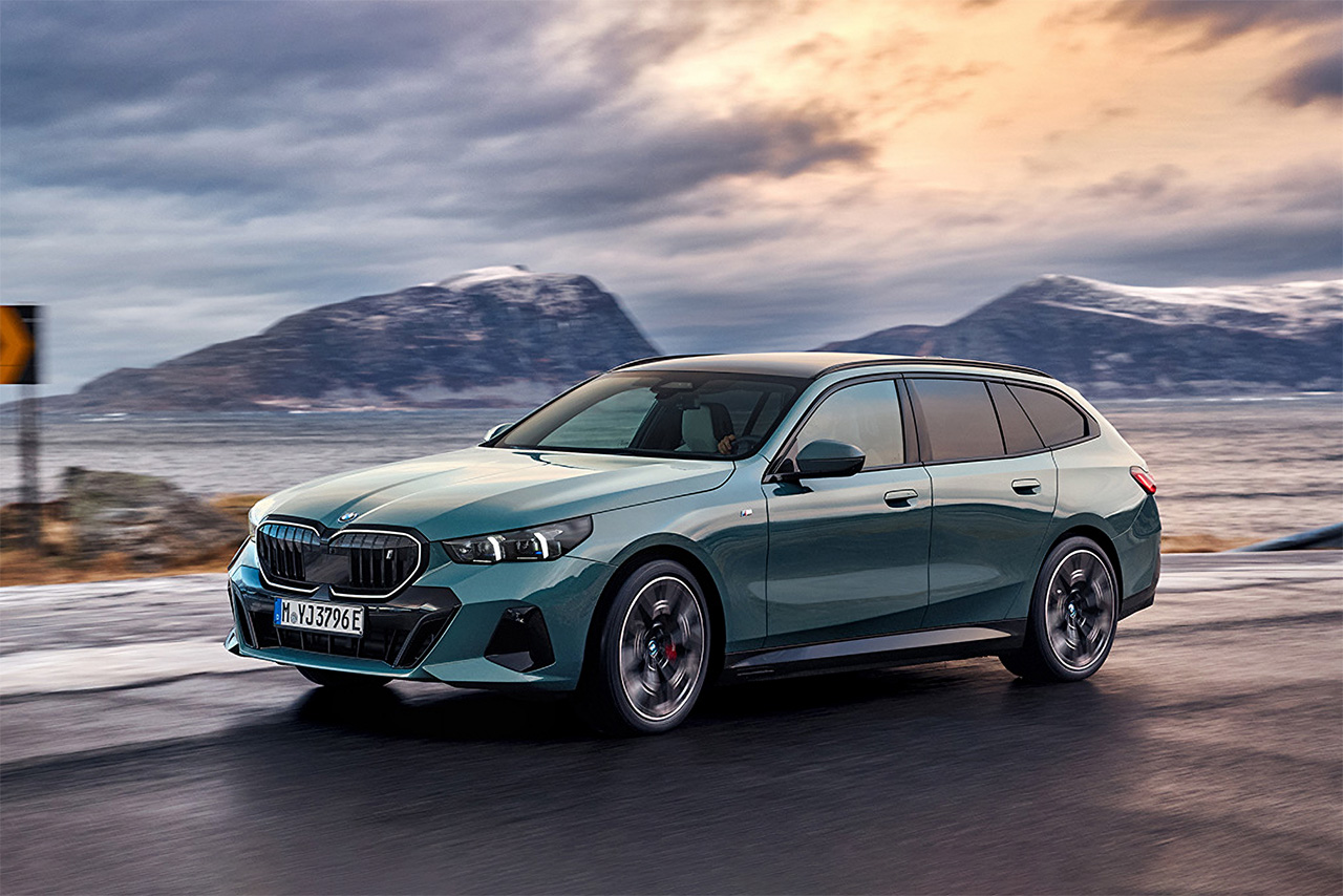 BMW i5 Touring in Sophisto Gray metallic drives along the sea.