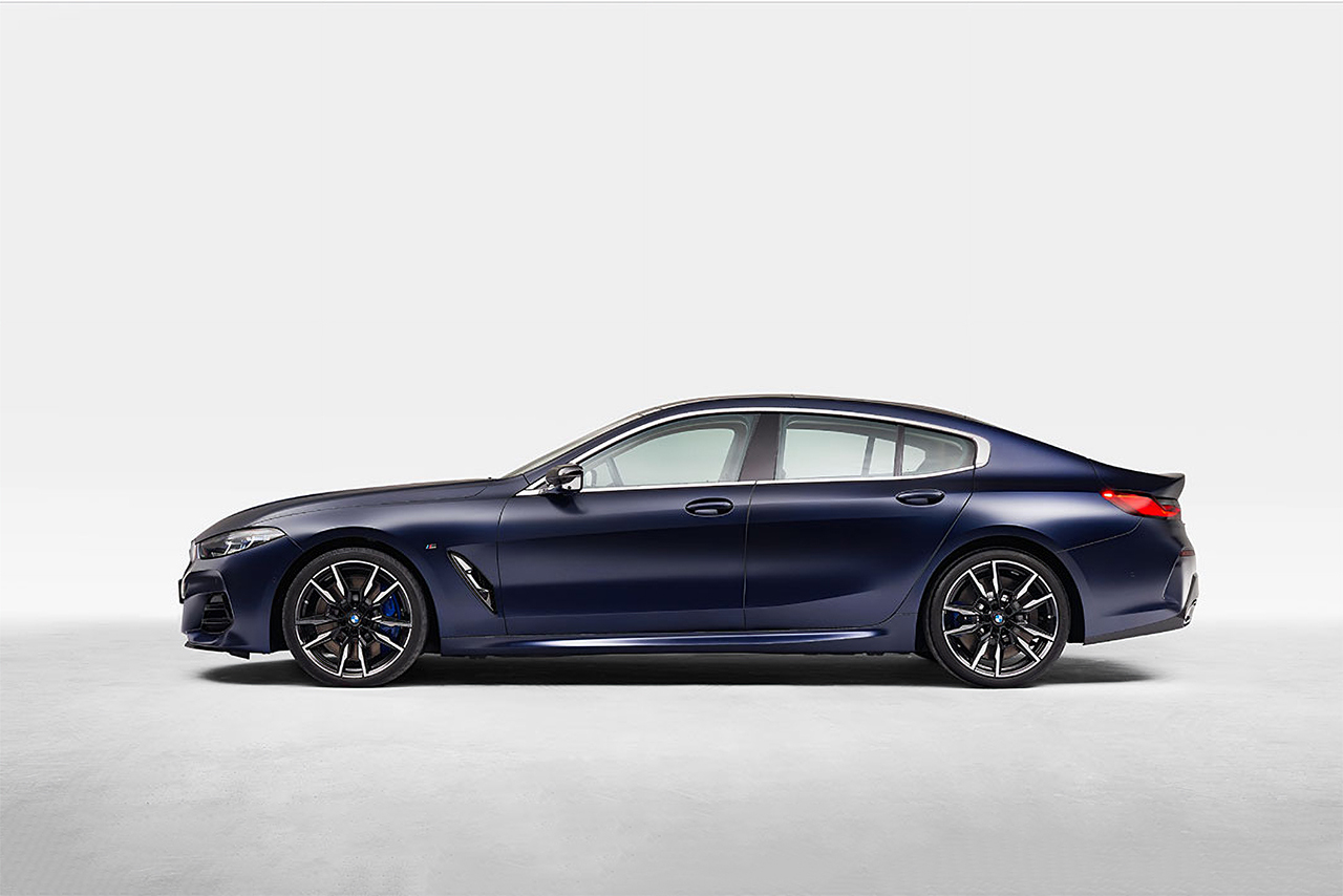 Dark blue BMW M8 Gran Coupé stands in a white room.