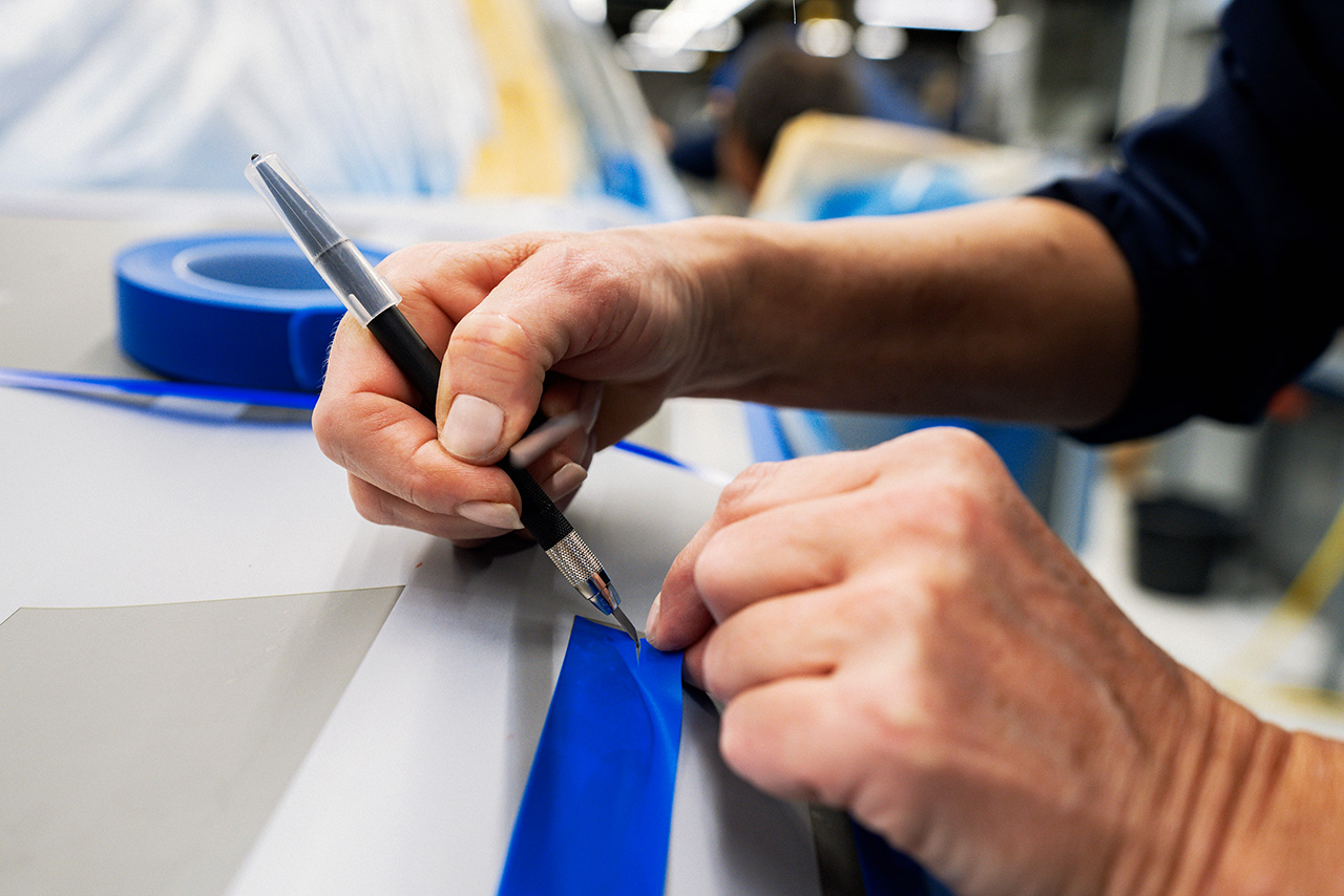 A BMW painter uses a utility knife to remove adhesive tape from a car.