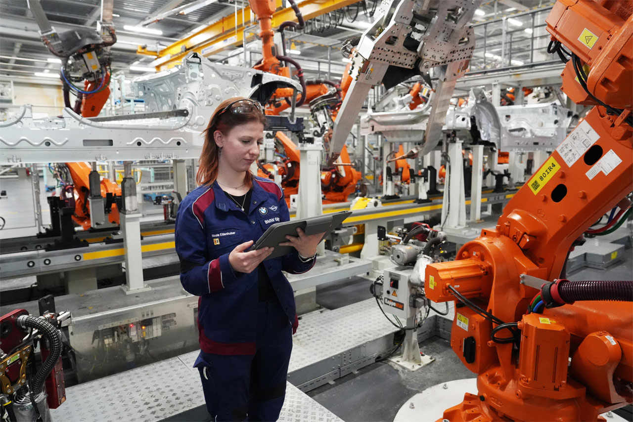 A woman in a blue uniform positions herself in front of a robot.