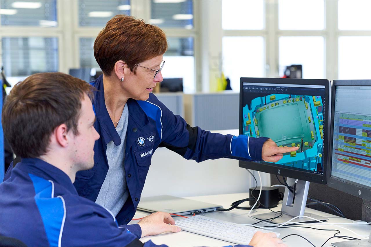 Zwei Mitarbeiter*innen unterhalten sich über einen auf dem Computerbildschirm dargestellten Plan.