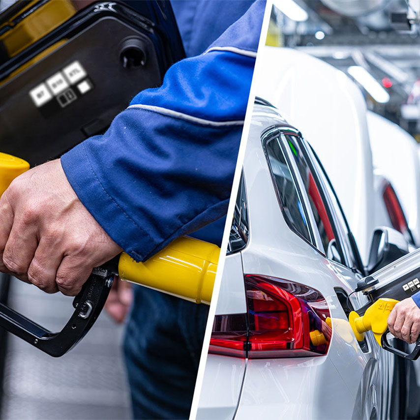 Nahaufnahme einer Person in blauer Arbeitskleidung, die eine gelbe Zapfpistole an einem weißen Auto hält.