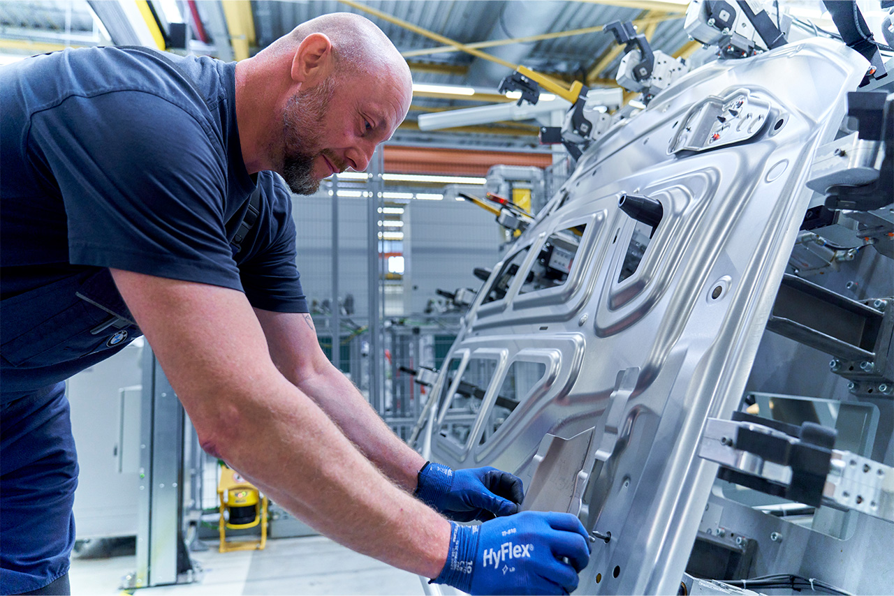 A parts manufacturing employee works on a metal part for a vehicle.