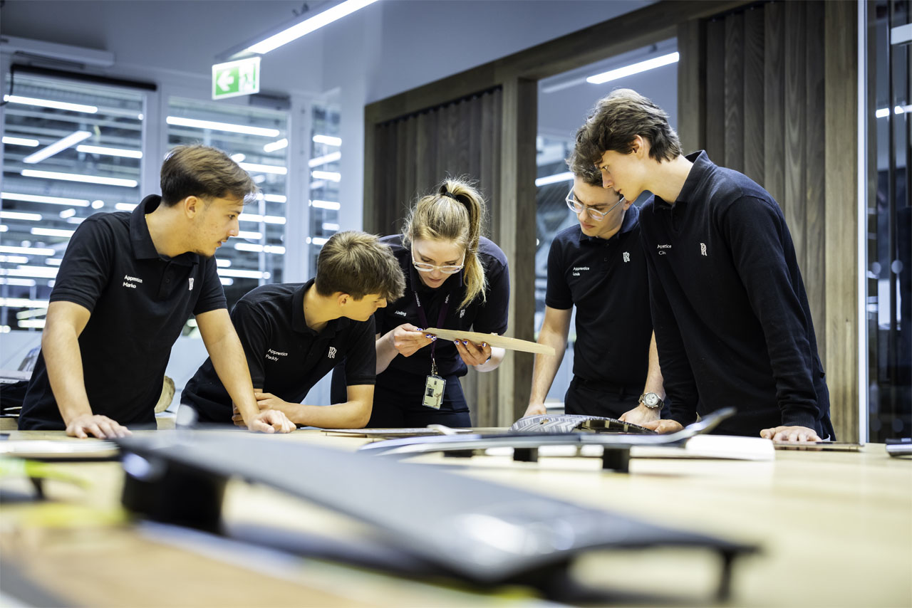 A diverse group of young people collaborating on a project at a table, surrounded by laptops and notebooks.