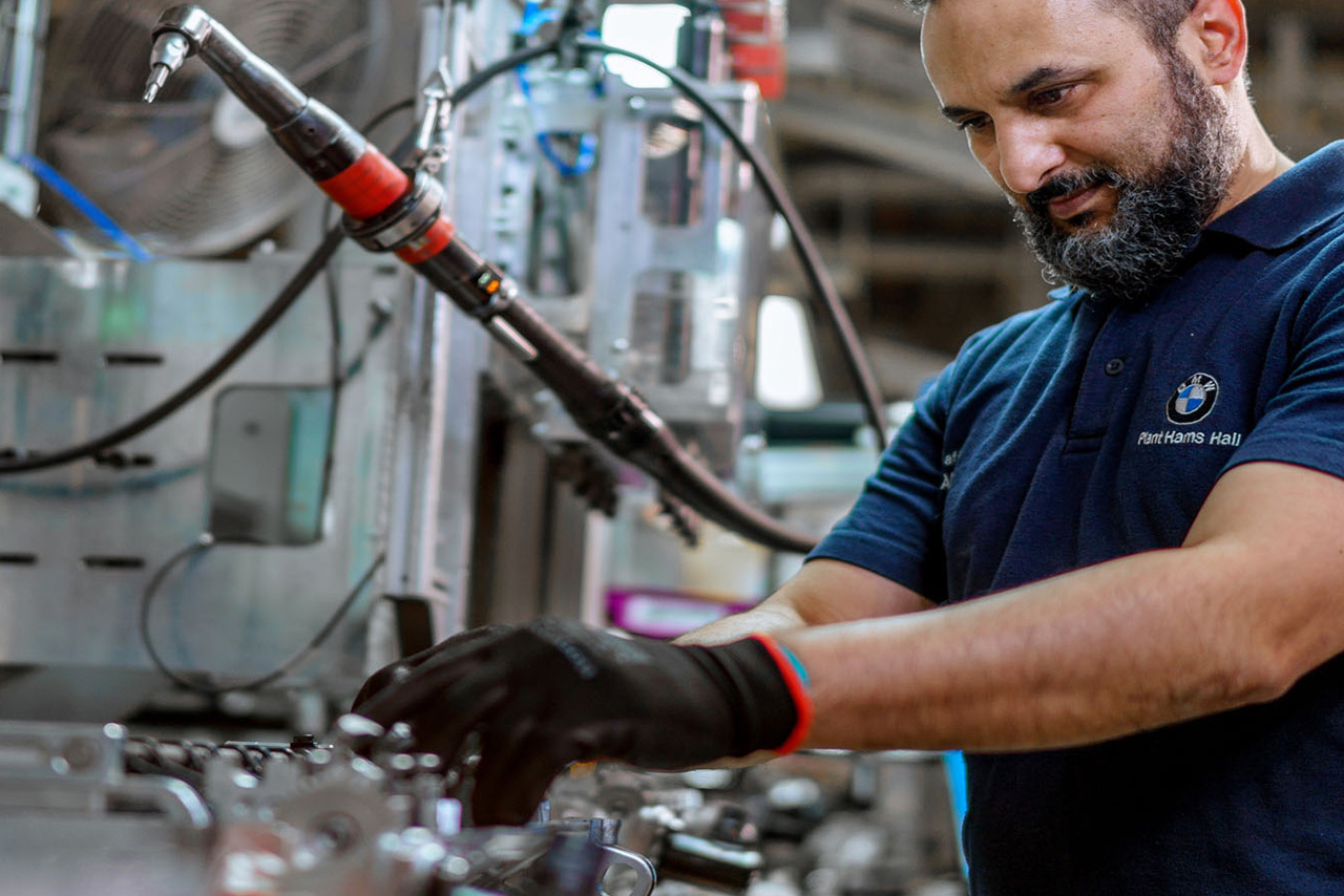 A man operates a machine in a factory, focused on his task amidst industrial equipment and surroundings.