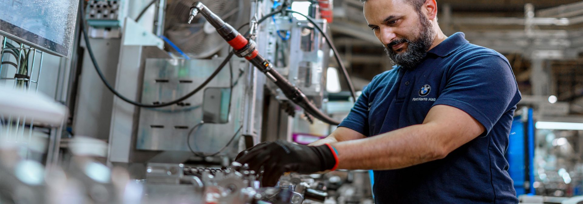 A man operates a machine in a factory, focused on his task amidst industrial equipment and surroundings.