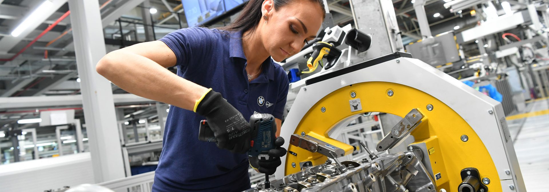 A woman works diligently on a factory machine, surrounded by industrial tools and equipment, showcasing her expertise.