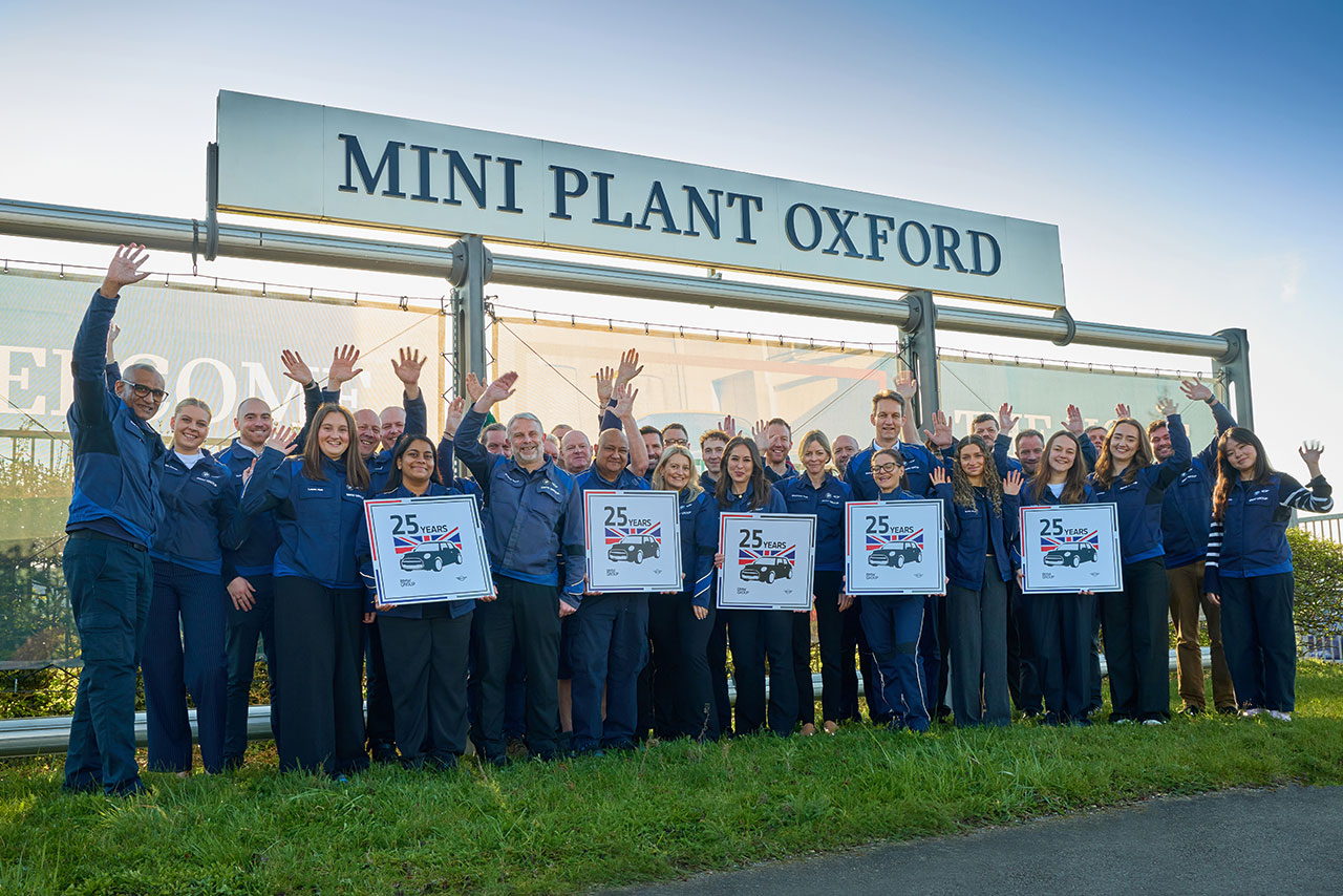 Group of people in front of a sign reading 'MINI PLANT OXFORD', some holding posters with '25' and raising their hands.