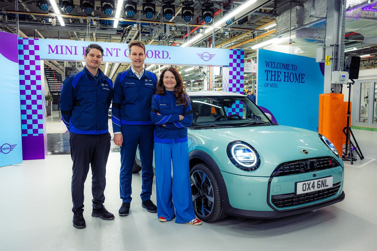 Three BMW employees are posing with a MINI vehicle that just rolled off the production line.