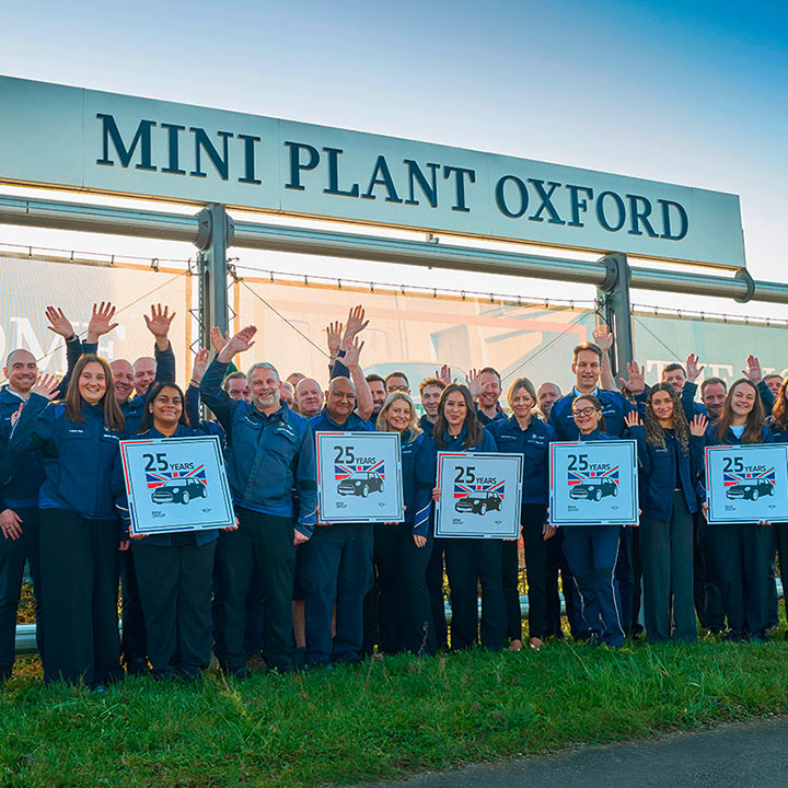 Group of people in front of a sign reading 'MINI PLANT OXFORD', some holding posters with '25' and raising their hands.