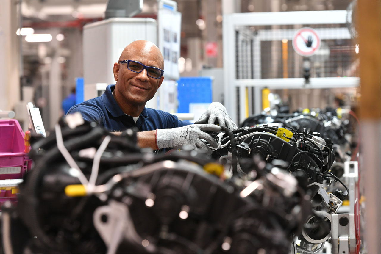 A man wearing a blue shirt and glasses is focused on repairing a car engine.