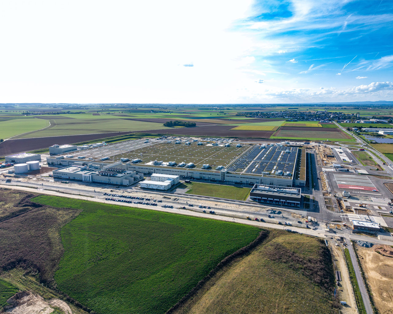 Luftaufnahme einer großen Industrieanlage mit mehreren Gebäuden, Tanks und Parkplätzen in einer ländlichen Umgebung.
