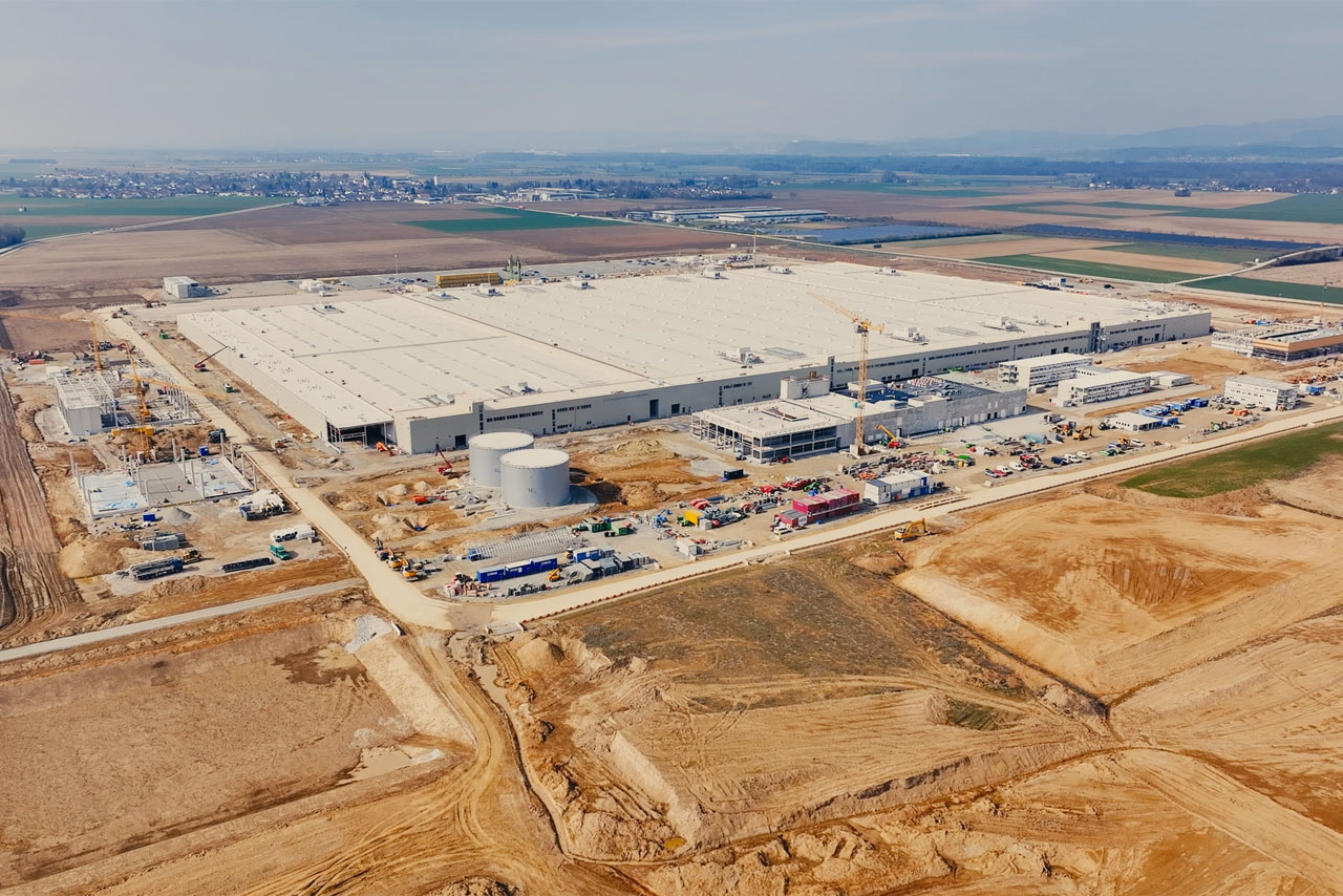Luftaufnahme einer Fabrik inmitten eines Feldes, umgeben von grüner Landschaft und landwirtschaftlichen Flächen.