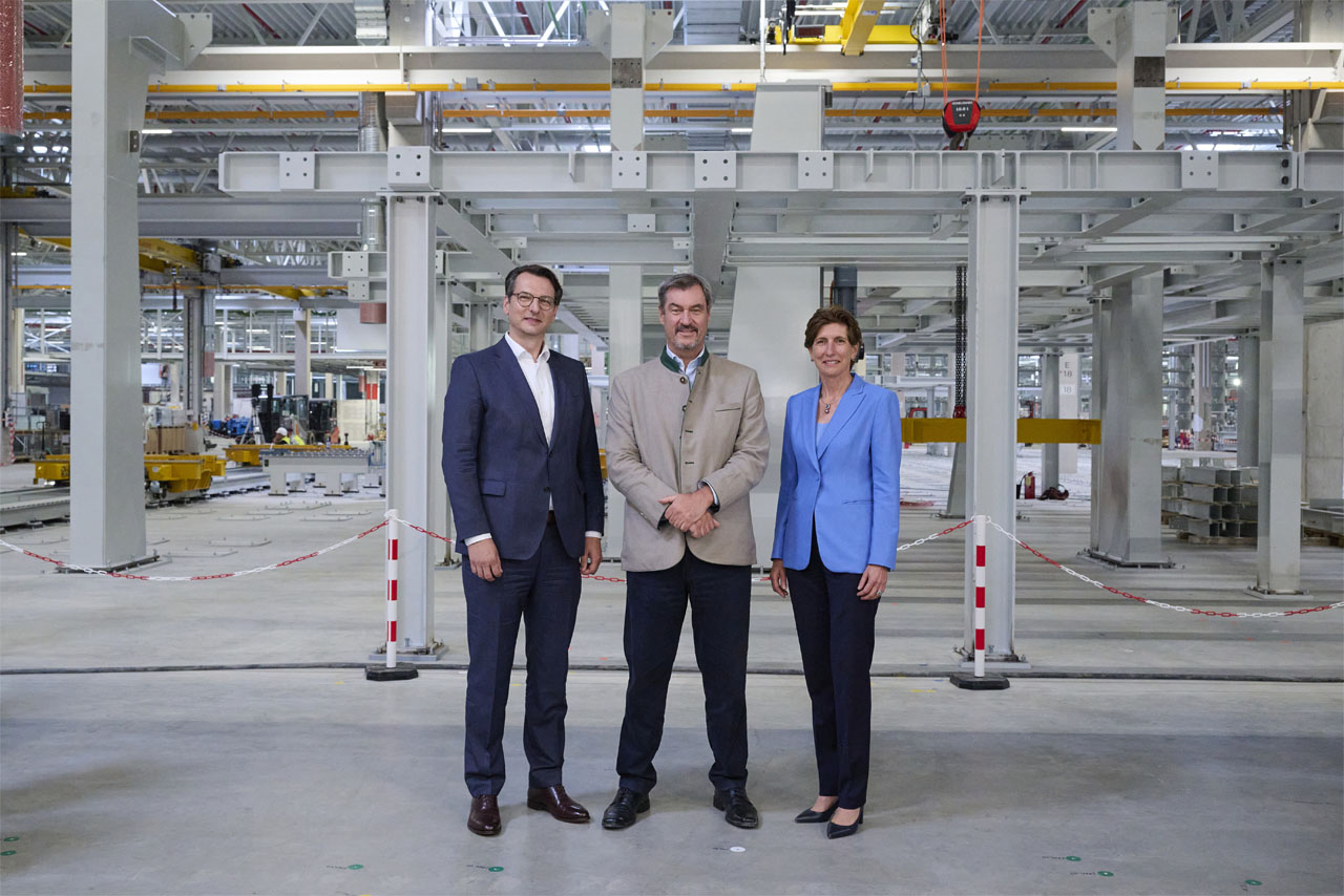 BMW Group Führung und Bayerns Ministerpräsident Markus Söder stehen in einem BMW Industriegebäude und betrachten die Umgebung.
