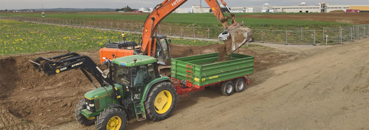 Auf einem Schotterweg sind ein Traktor und ein Lkw geparkt.
